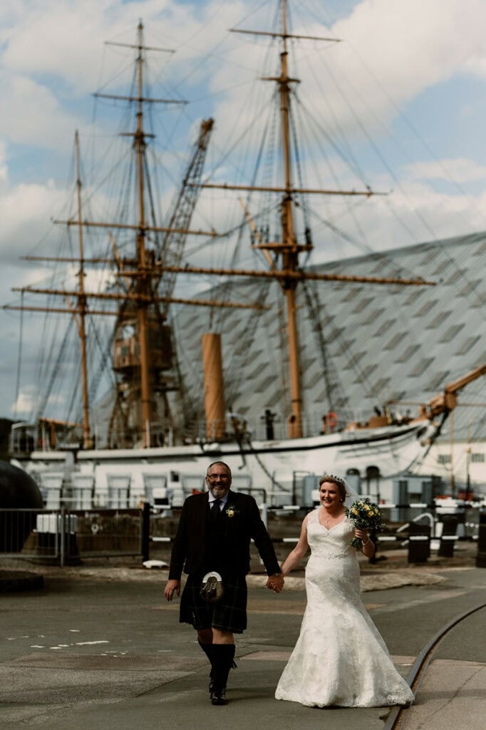 Bride and groom walking near historic ship.