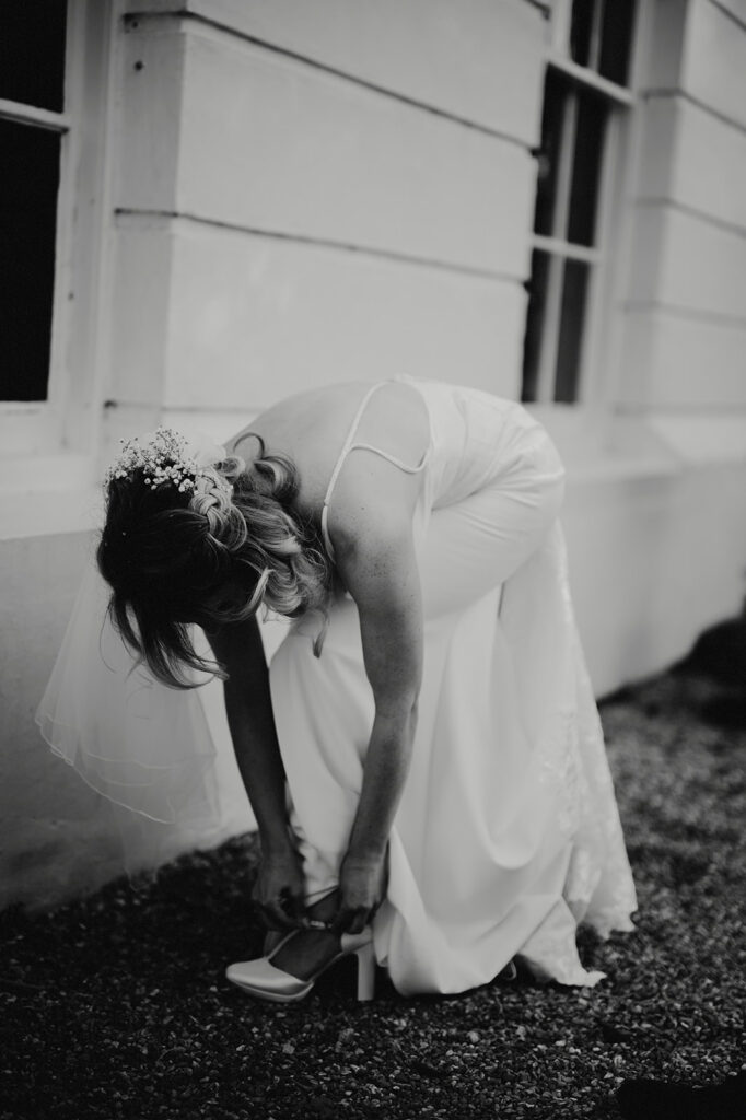 Bride in white dress adjusting her shoe.