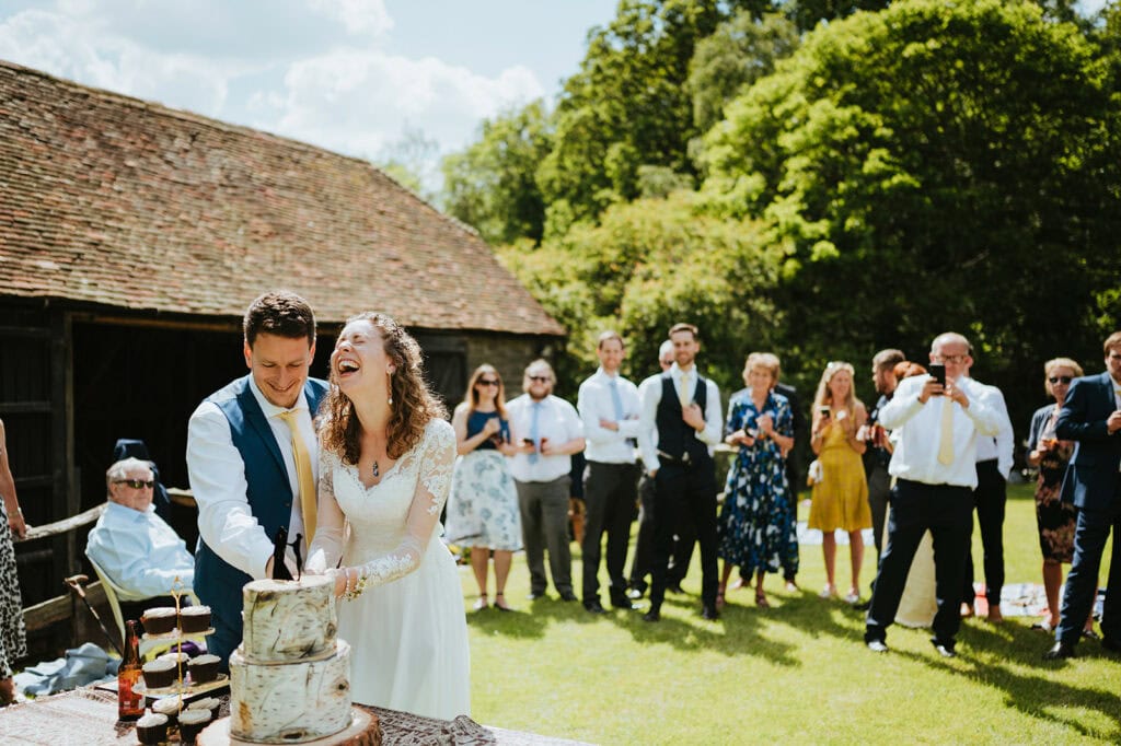 Wedding couple cutting cake outdoors, surrounded by guests.