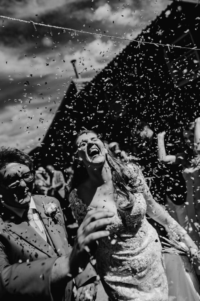 Bride and groom celebrating with confetti outdoors.