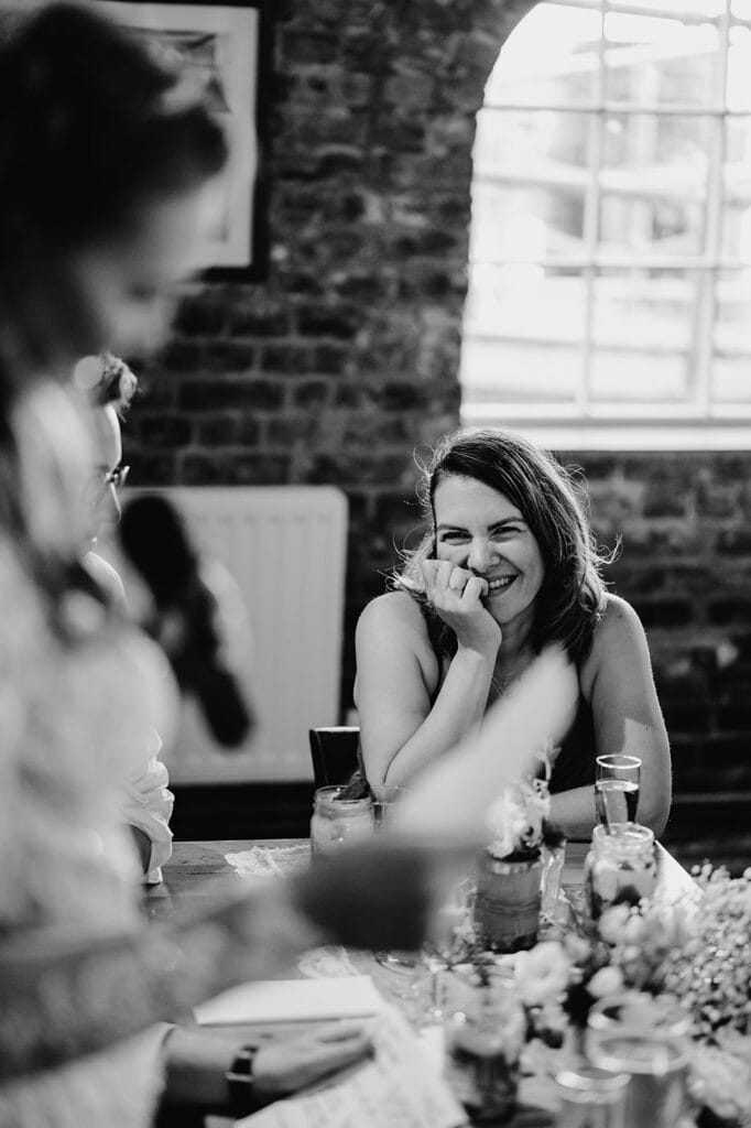Woman smiling during wedding speech in rustic venue.