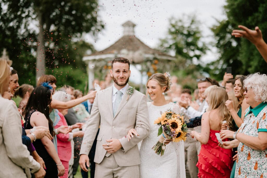 Newlyweds exit ceremony, guests celebrating with confetti.