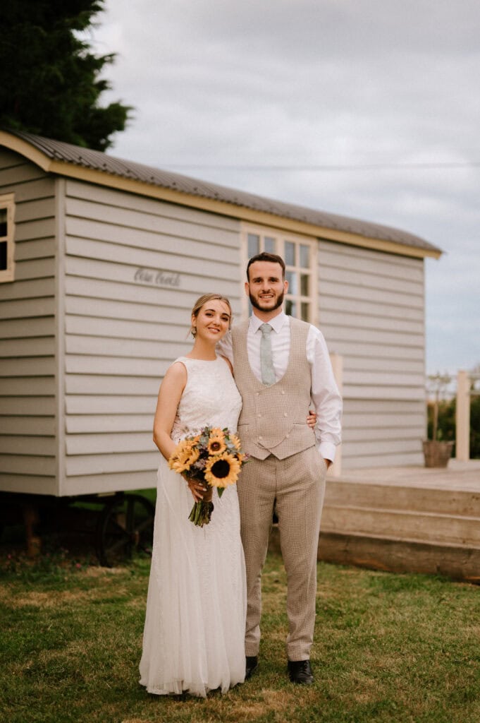 Bride and groom standing together, holding sunflowers.