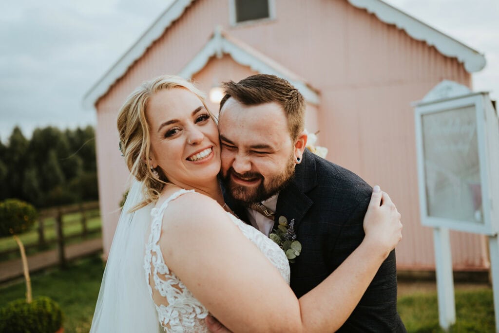 Bride and groom embracing at rustic wedding venue.