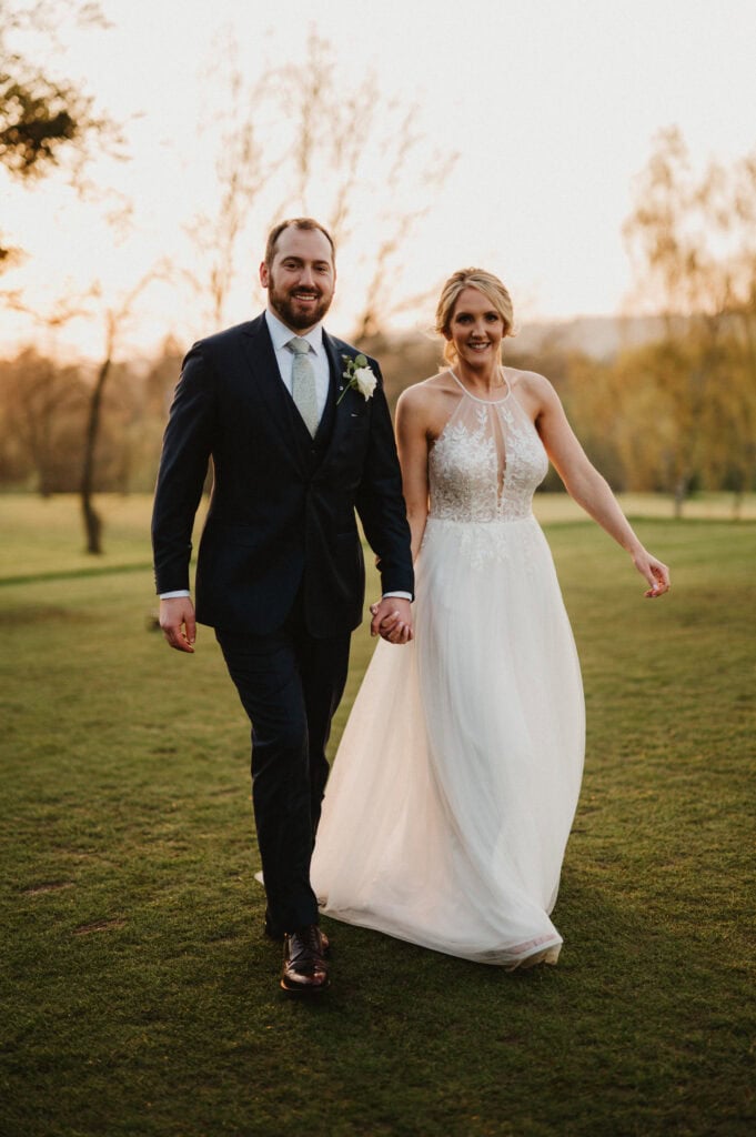 Bride and groom walking hand-in-hand in sunset.
