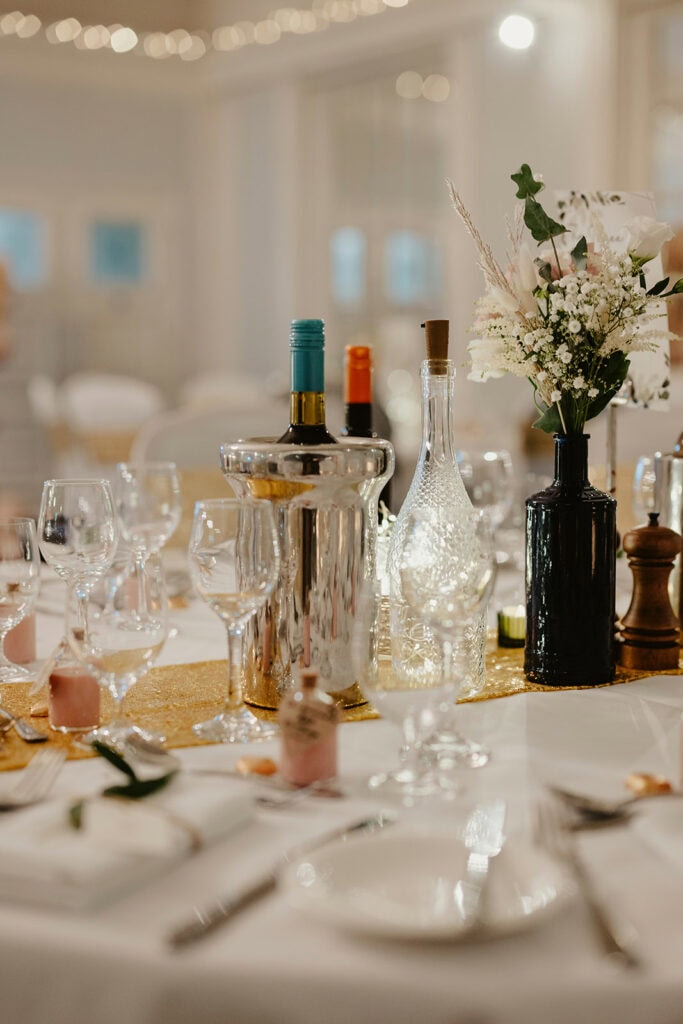 Elegant table setting with wine bottles, glasses, and floral centerpiece on a gold runner.