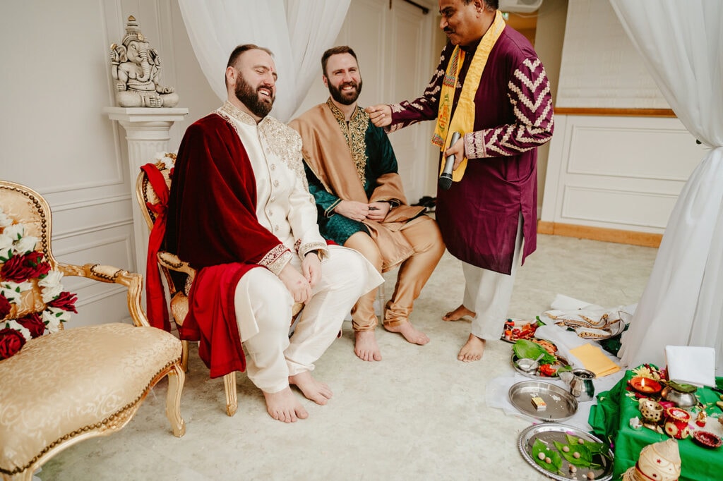 Three men are participating in a ceremonial event. Two men are seated on ornate chairs, dressed in traditional attire, while a third man stands next to them, engaging in the ceremony.