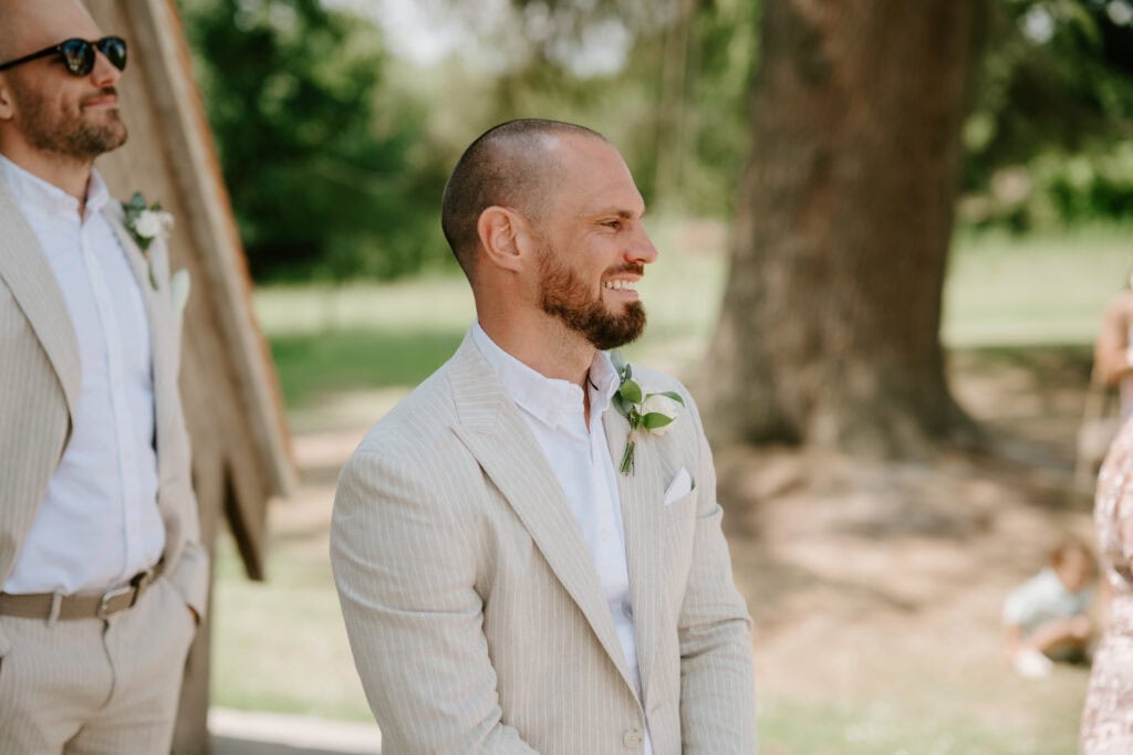 Smiling groom in light suit at outdoor wedding seeing his bride for the first time on wedding day