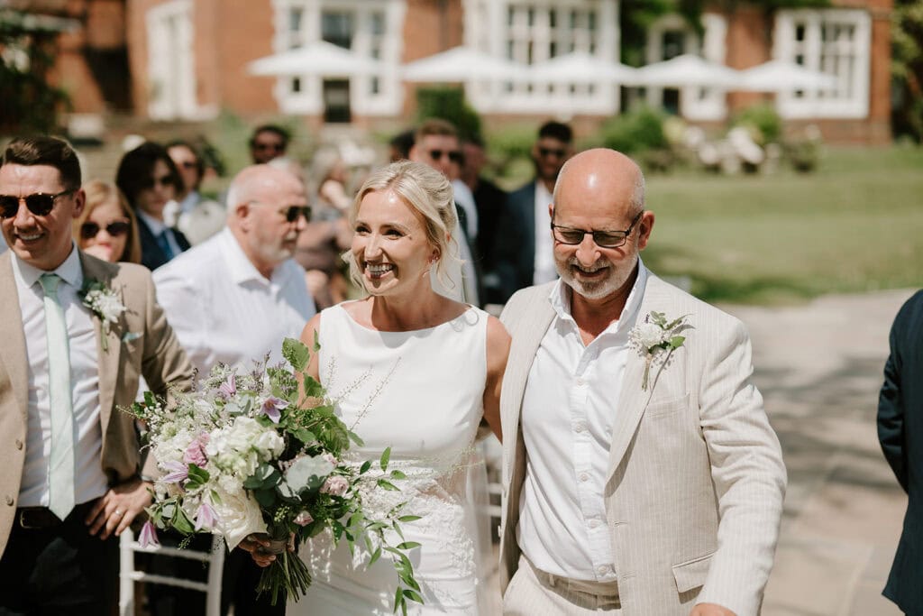 Bride walking down the aisle with father outdoors.