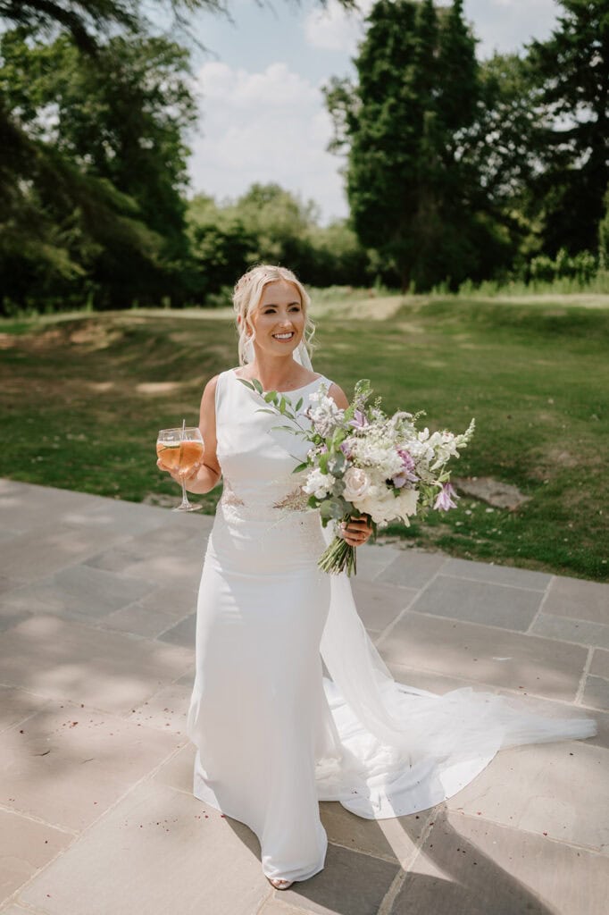 Bride holding bouquet and drink outdoors