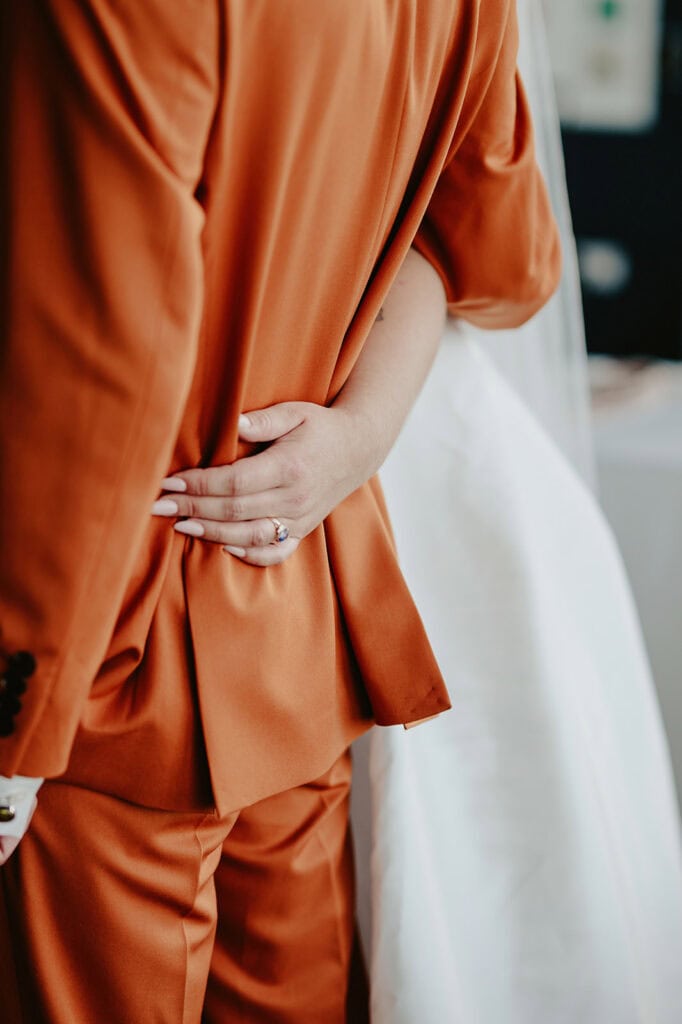 A person in an orange suit and a person in a white dress are embracing, with the focus on the hand on the back of the person in the suit.