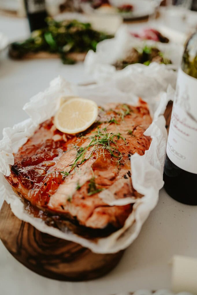 A cooked salmon fillet garnished with lemon slices and herbs on parchment paper, with a dark wine bottle beside it.