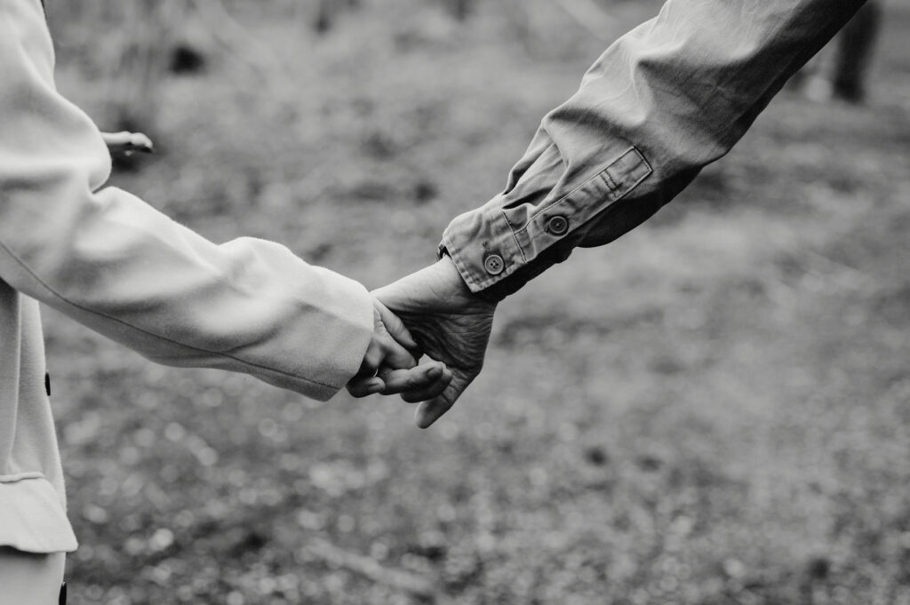 Two people holding hands outdoors, one wearing a light coat and the other in a darker jacket.