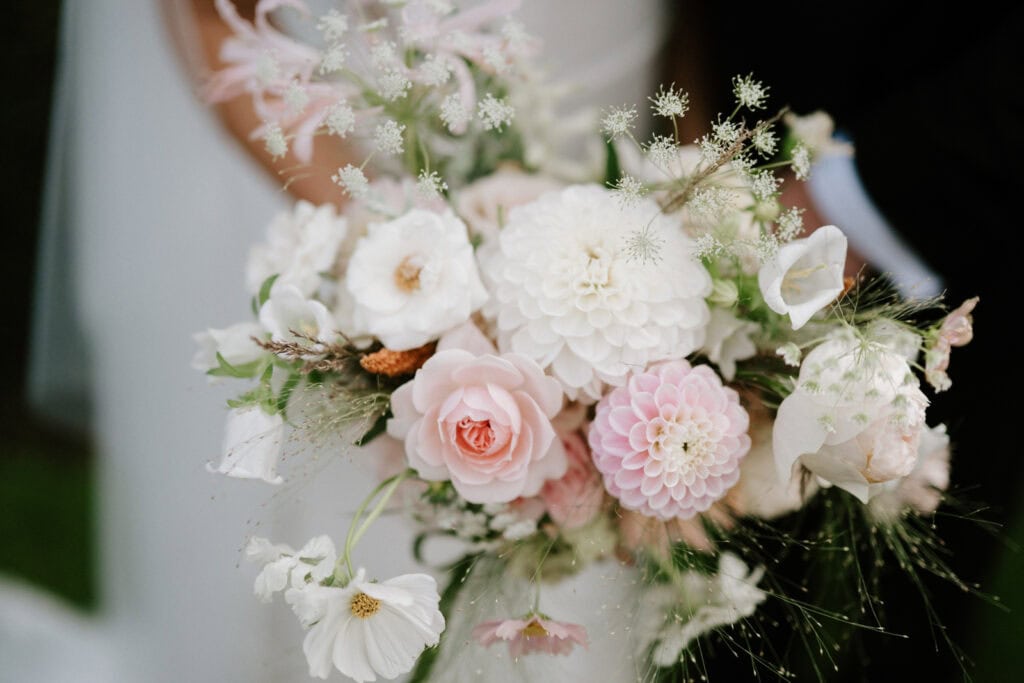 A close-up of a bouquet featuring pink and white flowers, including roses, dahlias, and cosmos, with greenery accents.