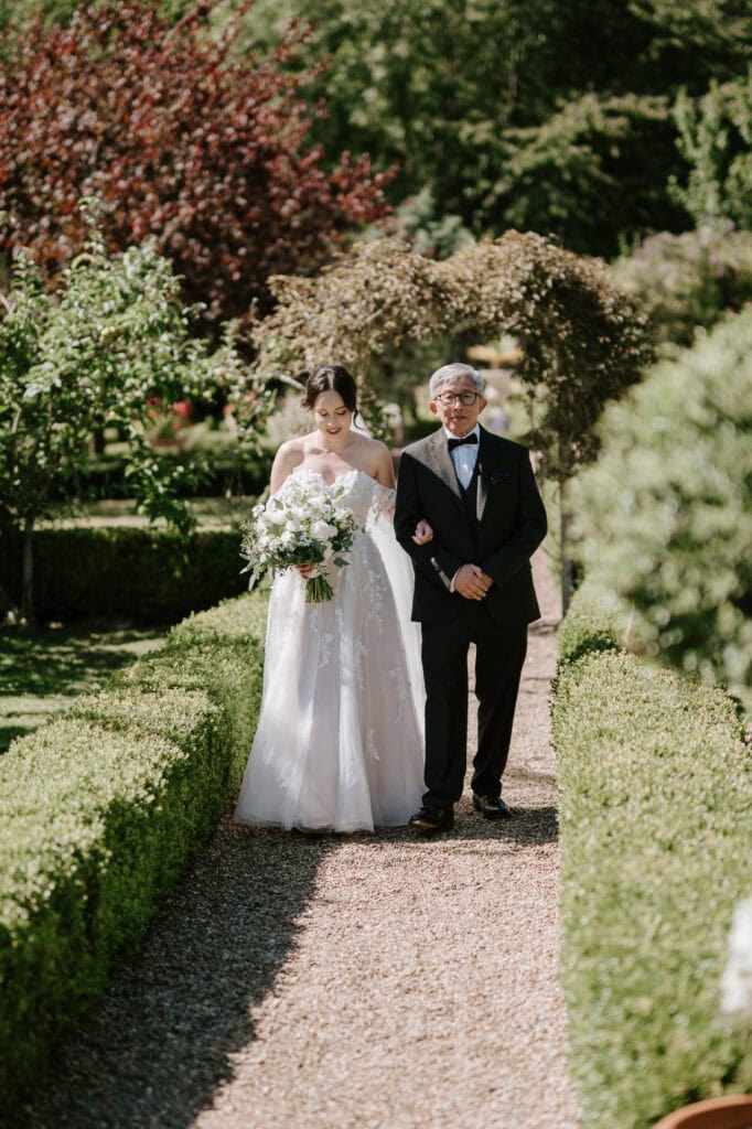 Bride walking down garden aisle with older man.