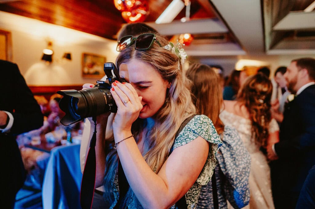 A person with long hair and a green floral dress is using a camera to take a photo at an indoor event.
