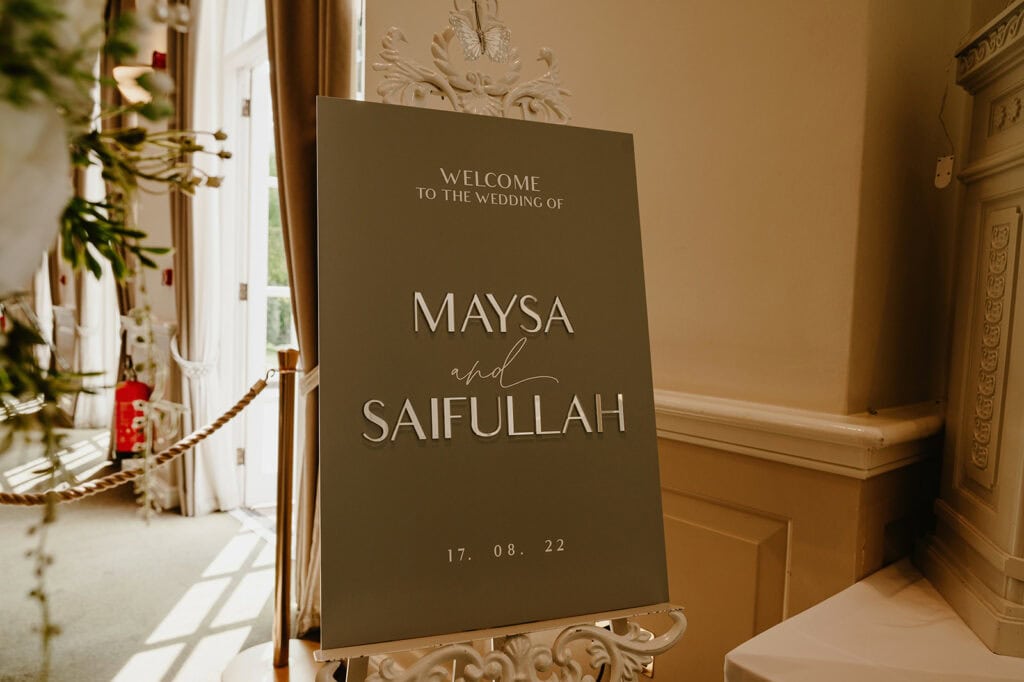 A wedding sign in an elegant setting reads, "Welcome to the wedding of Maysa and Saifullah, 17.08.22.