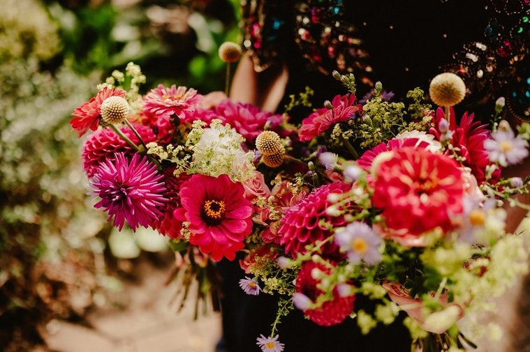 A florist in Kent is holding vibrant red and pink floral bouquets adorned with lush greenery in an idyllic outdoor setting.