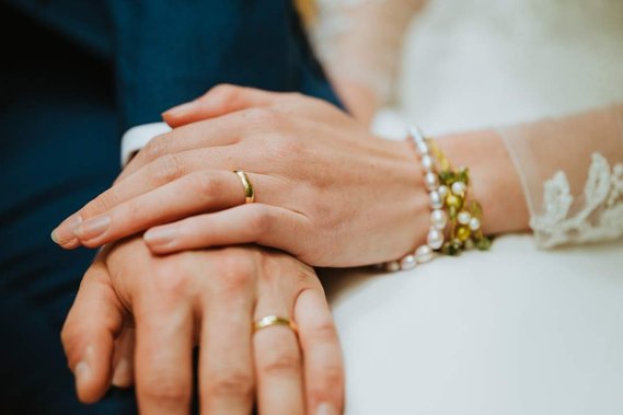 Close-up of two hands wearing wedding rings, one adorned with a pearl bracelet, set against a backdrop reminiscent of vintage fabric from an old Kent papermill.