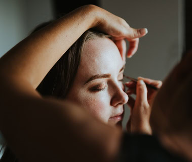 A person is having their eyebrows shaped by someone using a tweezer, preparing for a special event. Their eyes are closed, savoring the moment. A touch of elegance from London graces this intimate beauty ritual.