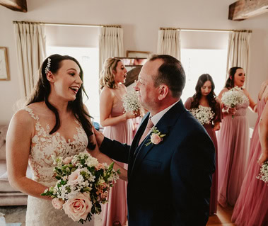 Bride on her wedding day smiling at her father with bridesmaids in the background at Pelham house