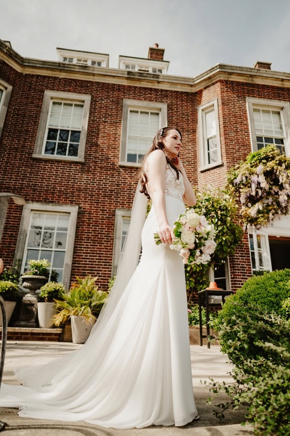 Stunning bride in very long wedding dress in a very cool pose holding her bouquet of flowers