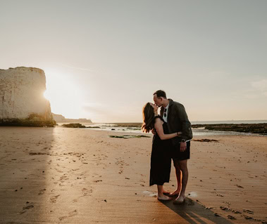 A couple stands on a sandy beach in Thanet at sunset, kissing and embracing each other—captured perfectly in stunning photography.
