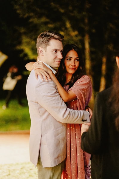 A couple embraces outdoors in the evening, with the man wearing a light suit and the woman in a pink dress, capturing the romance of a Kent wedding.