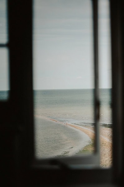 View of a beach and the sea from a window at Beacon House, focusing on two people walking along the shoreline in the distance, possibly enjoying a Kent wedding backdrop.