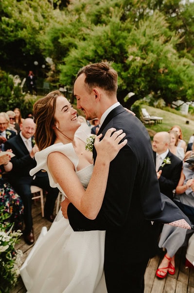 A couple dances joyfully, dressed in wedding attire, as guests look on and smile during an outdoor Kent wedding at the charming Beacon House.