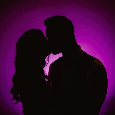 Silhouette of a couple kissing against a purple background, captured by a professional wedding photographer.