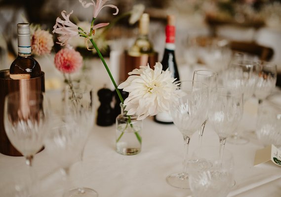 The wedding table set with numerous wine glasses, wine bottles, and flower decorations in small vases was a picturesque scene that any wedding photographer would love to capture.