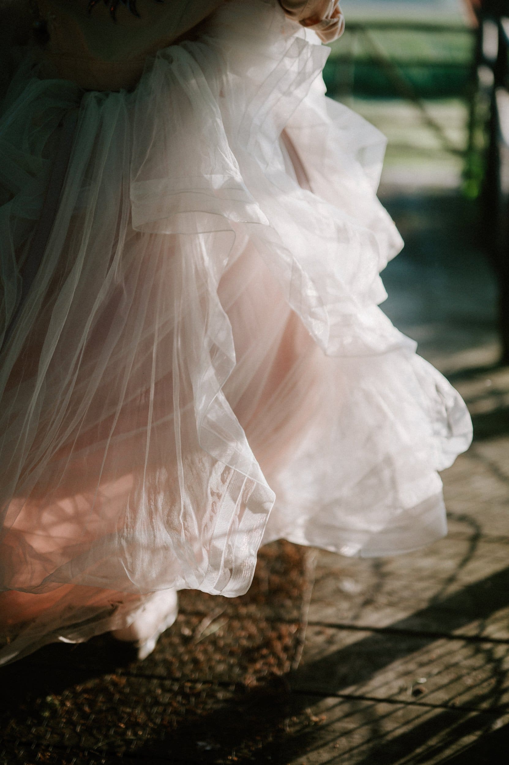 Close-up of a person wearing a flowing, white tulle dress, with sunlight casting shadows through the fabric, captured beautifully by a renowned Kent wedding photographer.