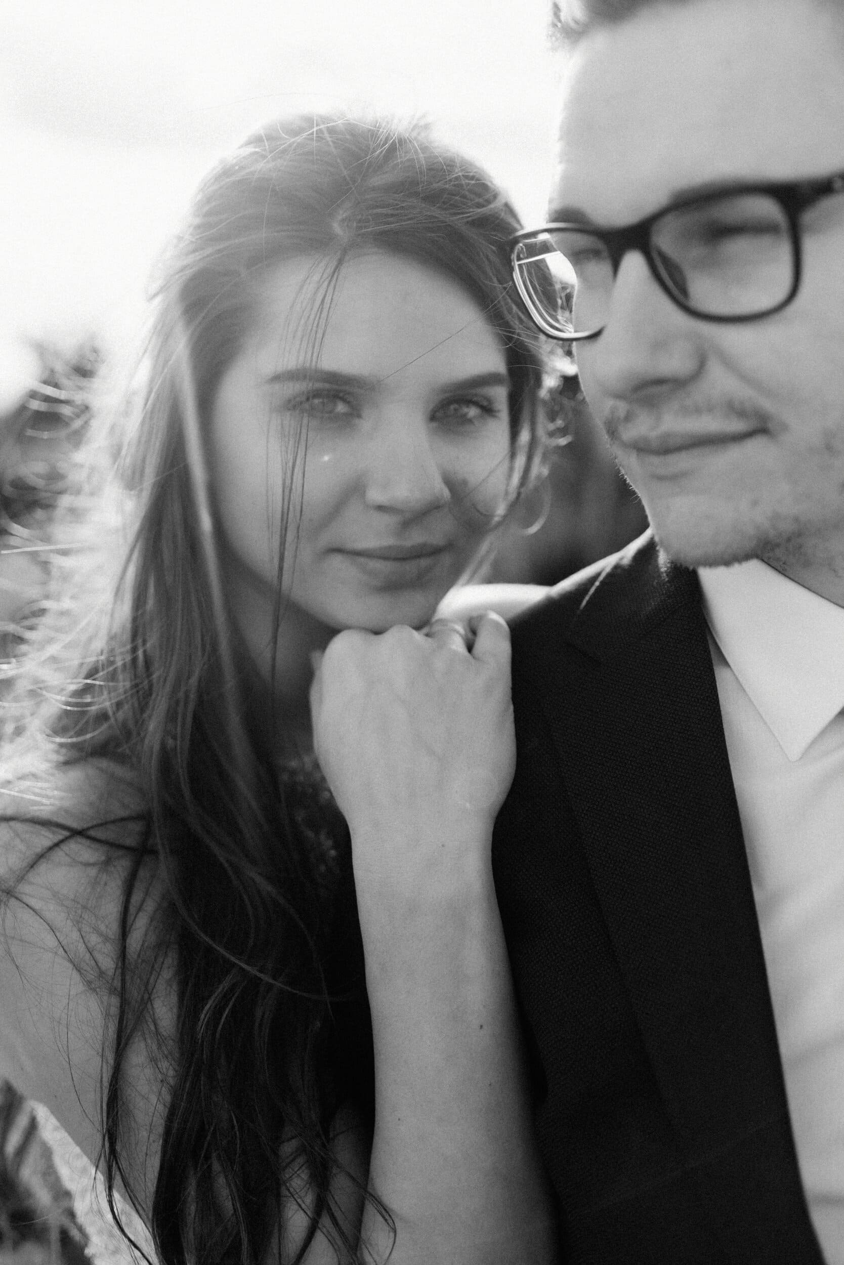 A wedding photographer captures a tender moment as a woman with long hair leans against a man in glasses and a suit in Kent. The man gently closes his eyes.