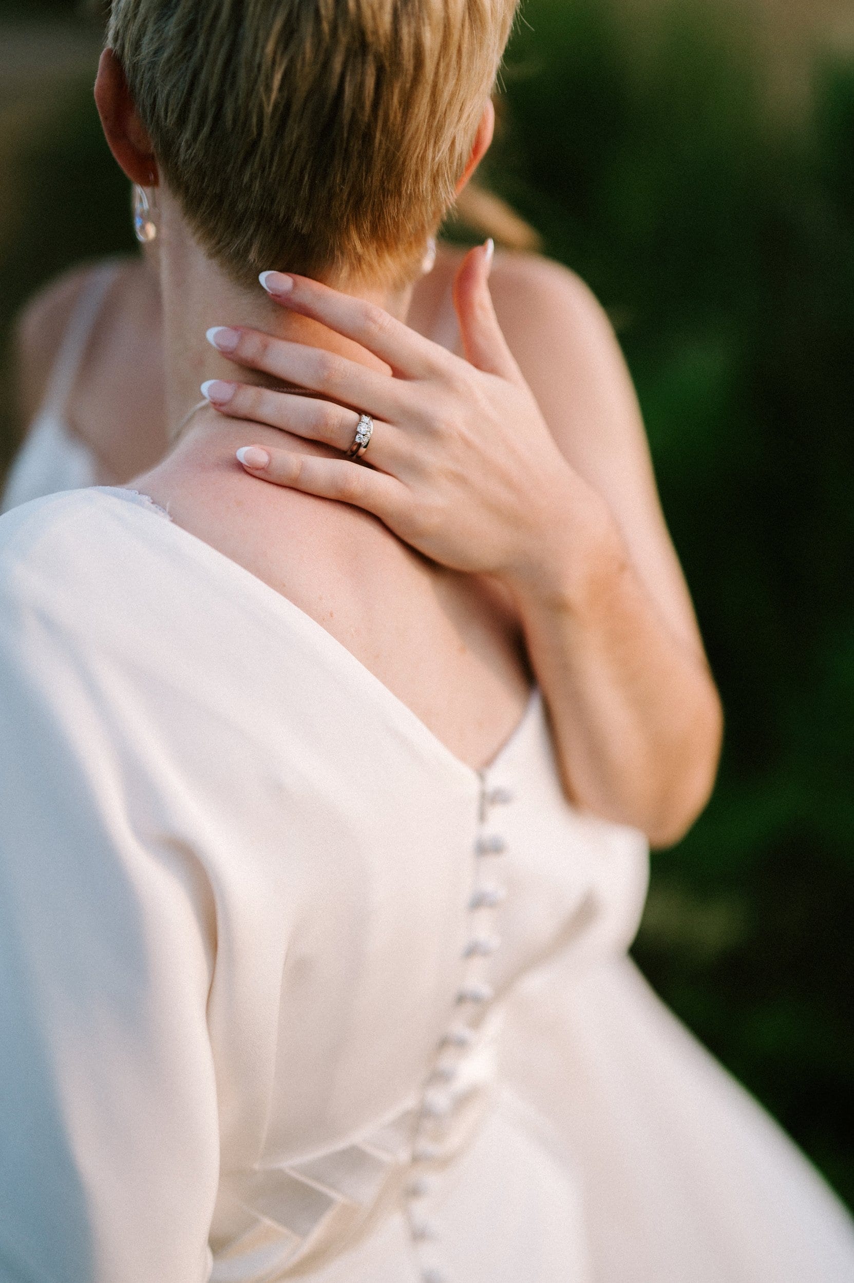 A person with short hair, wearing a wedding dress, is embracing another person with a hand adorned with a wedding ring on their shoulder, perfectly framed by a skilled Kent wedding photographer.