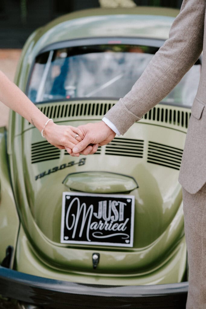 A couple holding hands in front of a green car with a "Just Married" sign attached to the rear.