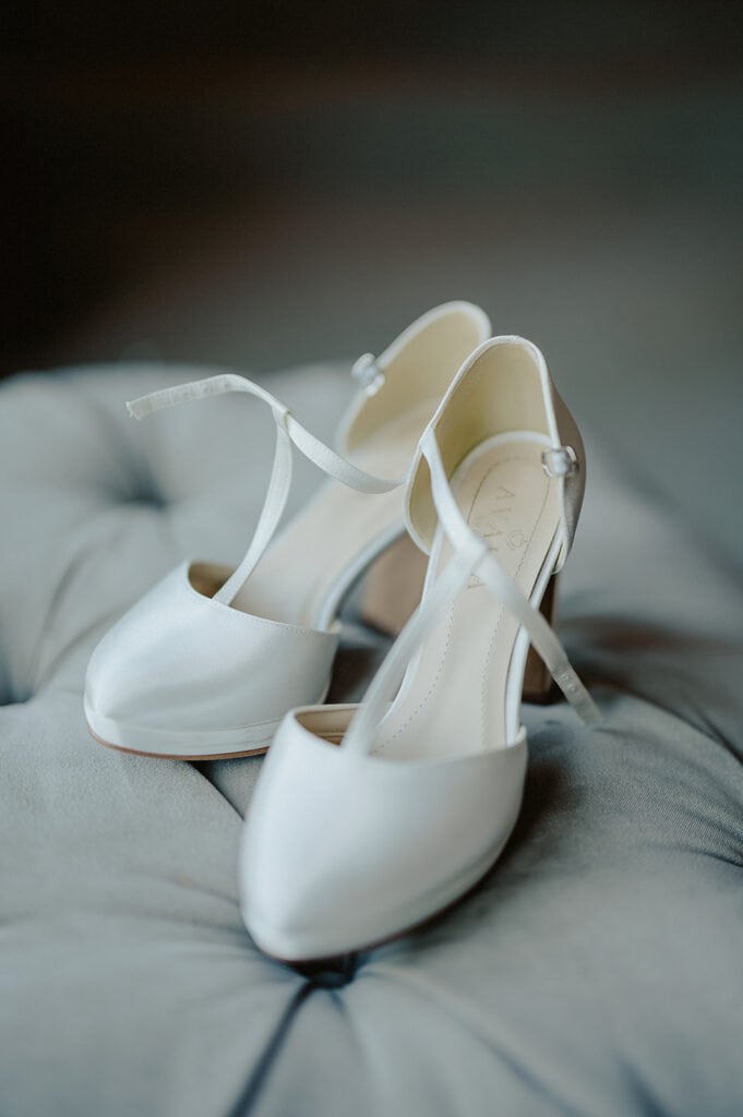 A pair of white high-heeled shoes with ankle straps placed on a cushioned surface.