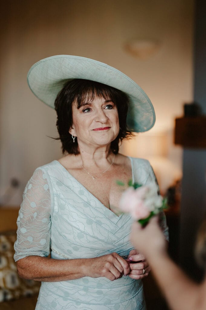 A woman in a light blue dress and matching wide-brim hat is looking off-camera while holding a pink corsage.