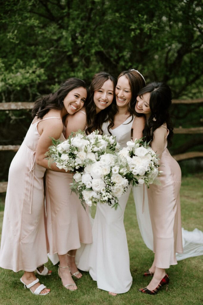 Bride with bridesmaids holding white flower bouquets outdoors.