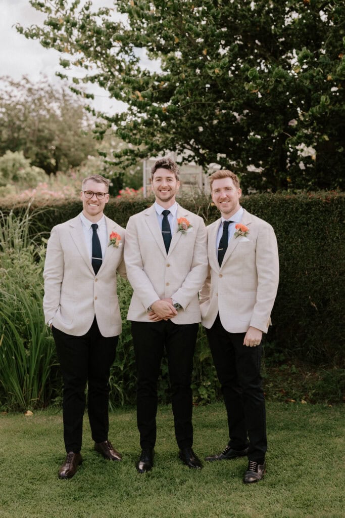 Three men in wedding attire standing in a garden.