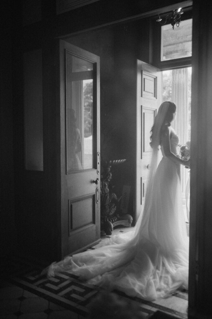 A bride standing in a doorway, black-and-white photograph.
