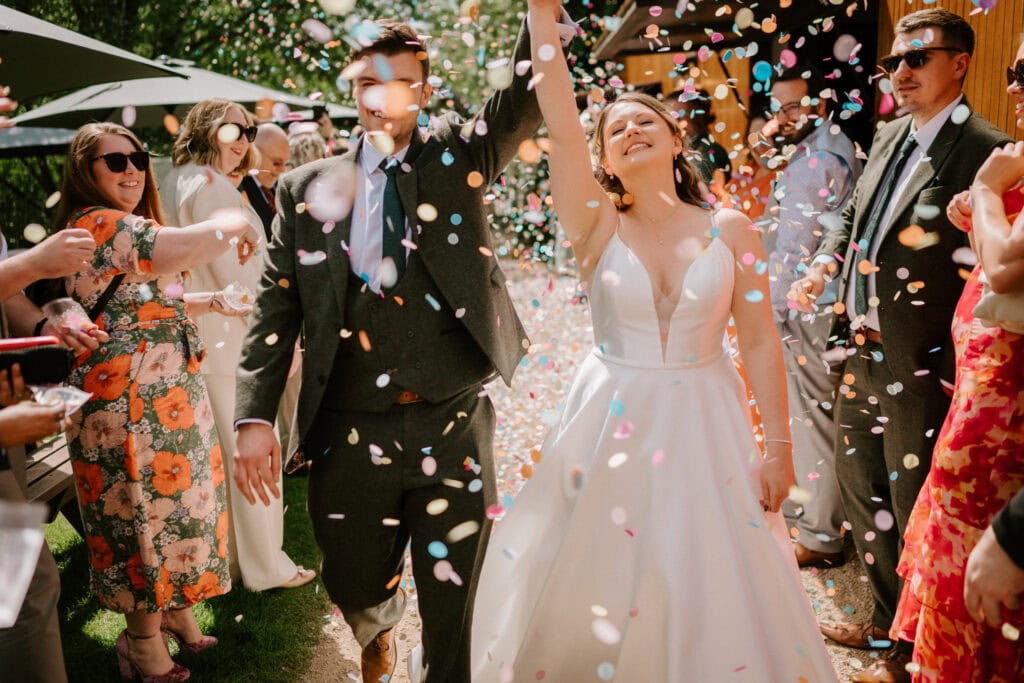 Newlyweds celebrating under colourful confetti at outdoor wedding.