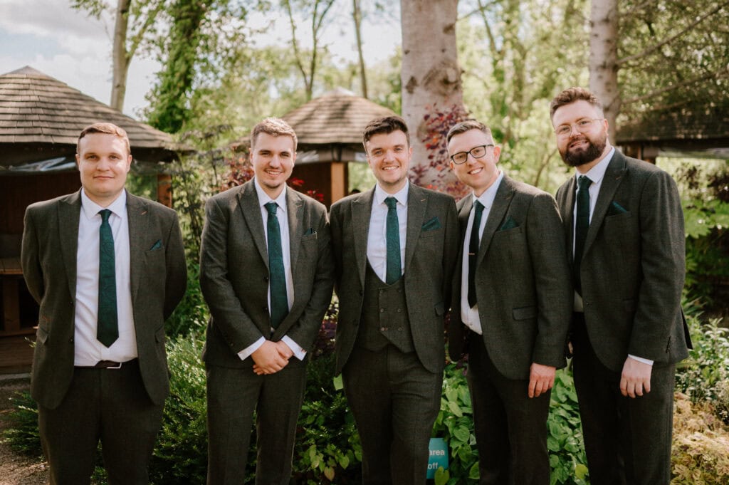 Groomsmen in suits posing outdoors at a wedding.