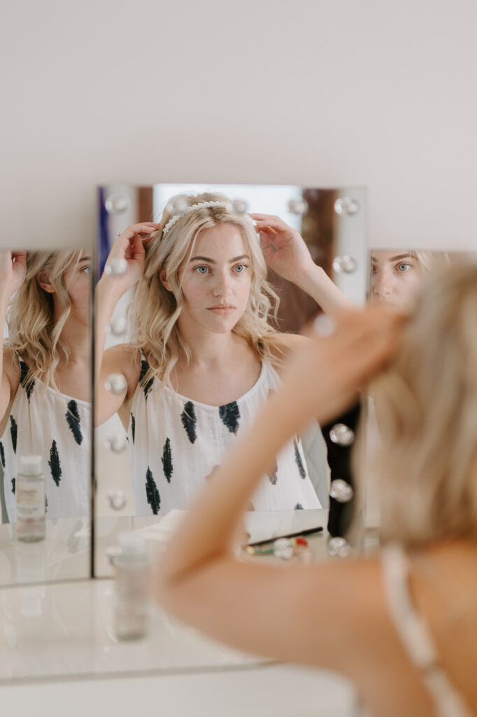 Woman adjusts headband in front of mirror.