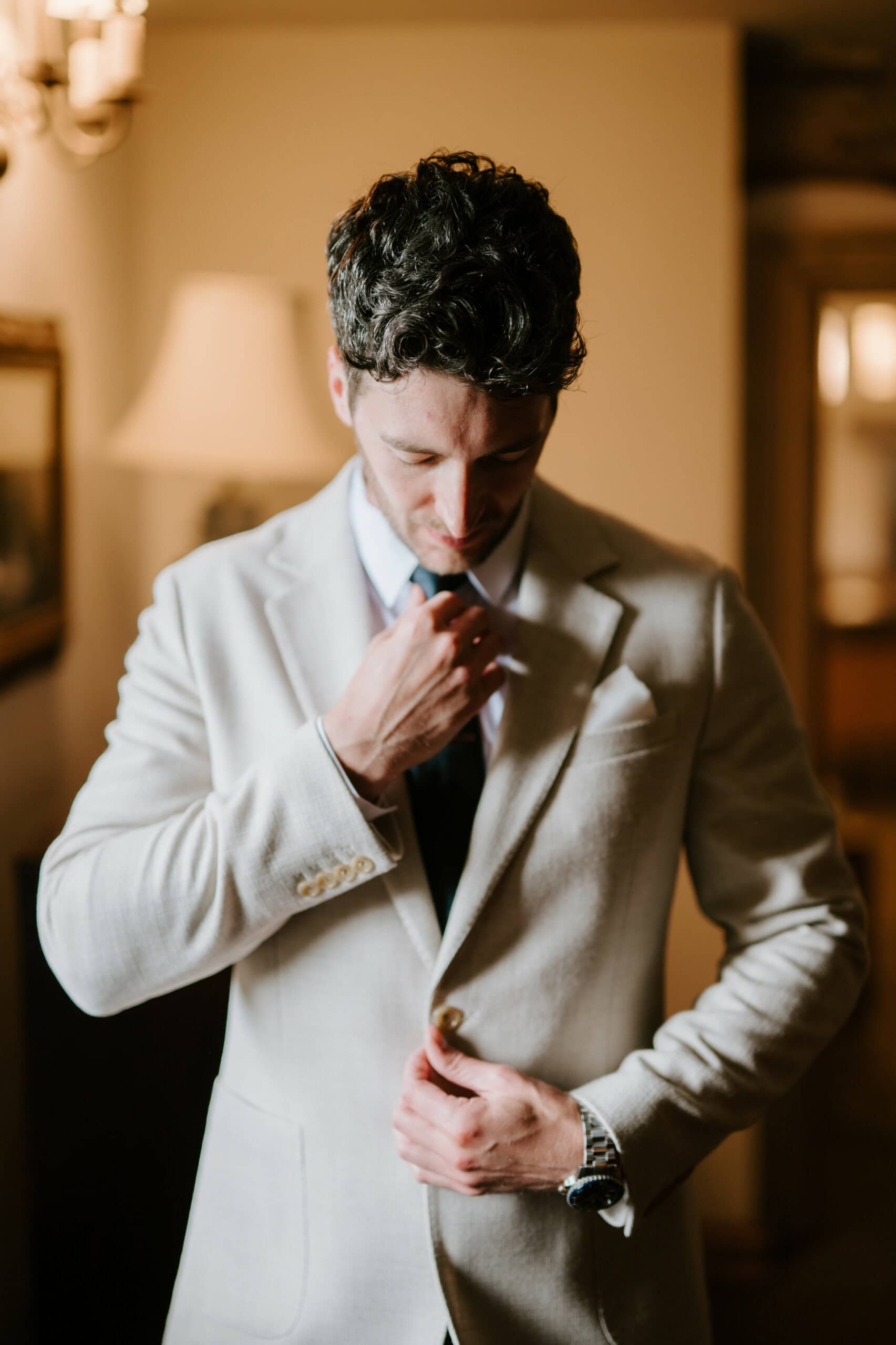 Man adjusting beige suit jacket indoors