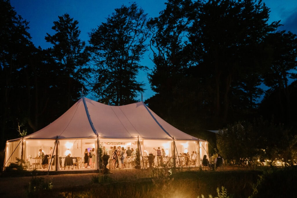 Evening wedding reception under a tent with lights.