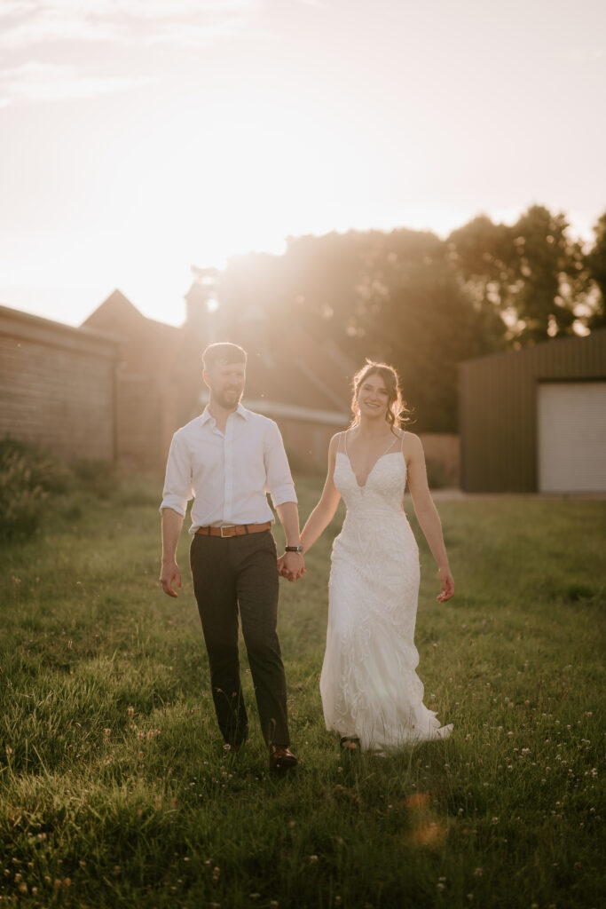 Bride and groom walking in a field at sunset