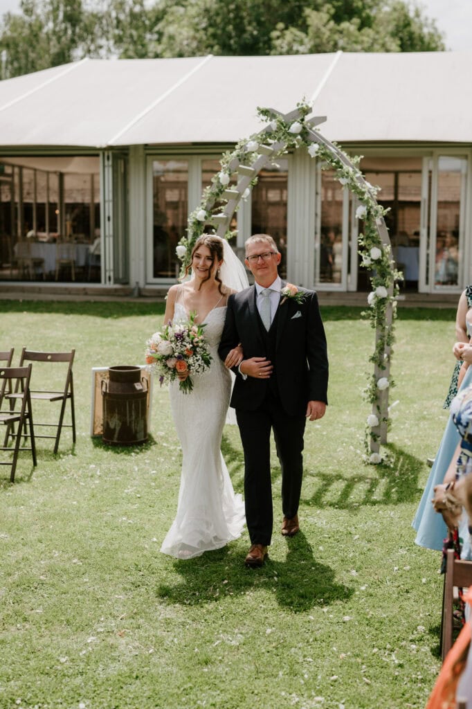 Bride and father walking down the aisle outdoors.