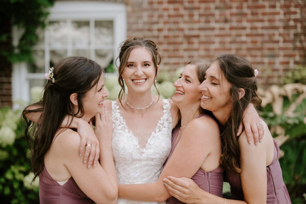 Bride and bridesmaids in lavender dresses smiling outside.