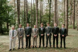Groomsmen standing in forest wearing suits.